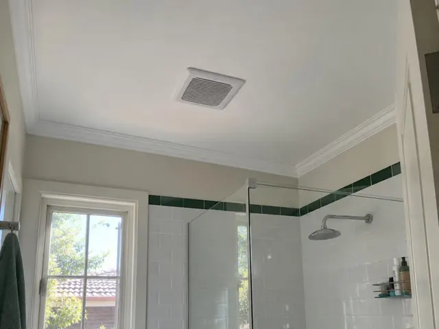 Bathroom ceiling exhaust fan above tiled shower and white ceiling with cornice in Pymble