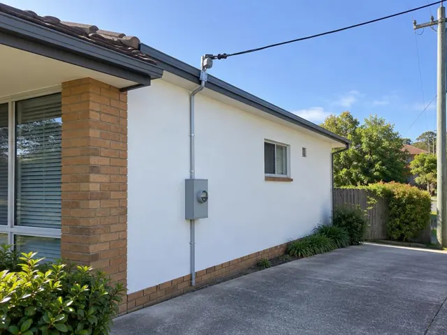 White suburban house exterior with overhead service cable and point-of-attachment bracket on the wall in St Ives
